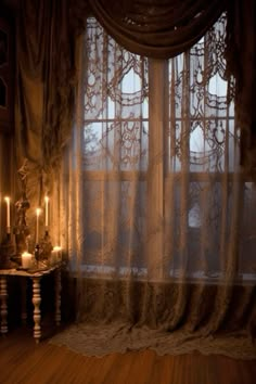 a window with sheer curtains and candles in front of it, on a wooden floor