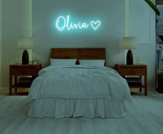 a bed with white sheets and pillows in a room that has neon lights on the wall above it