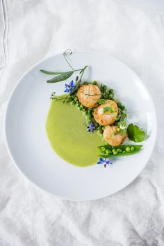 a white plate topped with green sauce and shrimp on top of pea puree next to peas