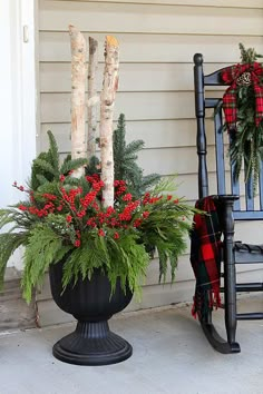 a rocking chair sitting next to a planter filled with red berries and greenery