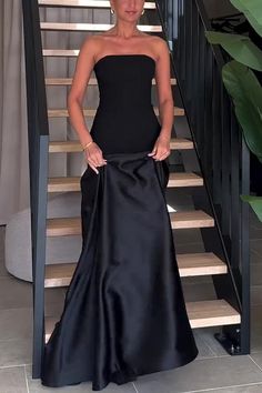 a woman in a black dress standing next to a stair case with her hands on her hips