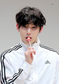 a young man brushing his teeth with an electric toothbrush while wearing a white adidas jacket