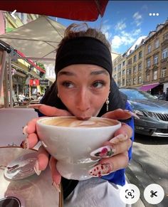 a woman drinking from a white cup on top of a table