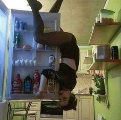 a woman is upside down in the kitchen while doing a handstand on an open refrigerator