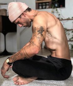 a shirtless man sitting on the floor with his hands in his pockets and wearing a pink beanie