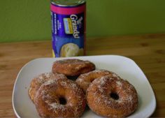 three donuts on a white plate next to a can of lemonade and some powdered sugar