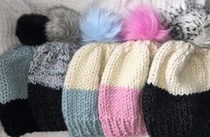 several knitted hats are lined up on a white blanket with different colored pom - poms