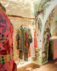 clothes are hanging on the rack in front of a wall with an exotic design and palm tree