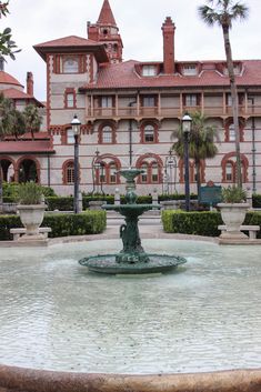 a fountain in front of a large building with palm trees around it and two lamps on each side