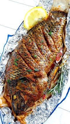 a fish is on foil with lemon wedges