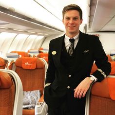 a man in a suit and tie standing on an airplane with orange seats behind him