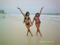 two women in bikinis on the beach with their arms up and legs spread out