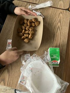 a person holding a bowl filled with food on top of a wooden table next to plastic bags