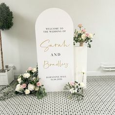 a welcome sign with flowers and greenery next to it on a tiled floor in front of a white wall