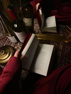 a person sitting on the floor reading a book next to some wine bottles and a lamp