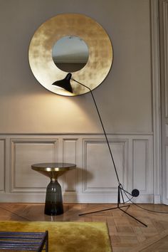 a round mirror sitting on top of a wooden floor next to a lamp and table