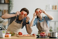 man and woman in aprons holding up tomatoes to their eyes