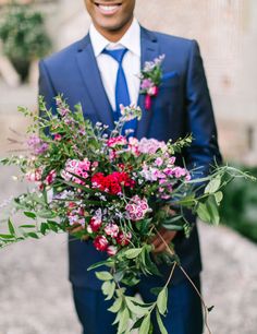 a man in a blue suit holding a bouquet of flowers and greenery on his arm