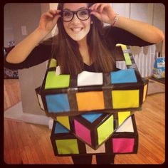 a woman in glasses is holding up a rubikt cube shaped bag that she made out of cardboard