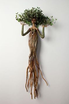 a woman with long hair and green leaves on her head is hanging from a wall