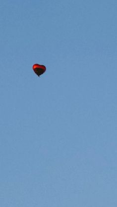 a red kite flying in the blue sky with a heart on it's tail