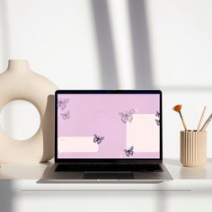 an open laptop computer sitting on top of a desk next to a vase and brush