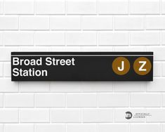 a black and white sign that says broadway street station j2 on the side of a brick wall