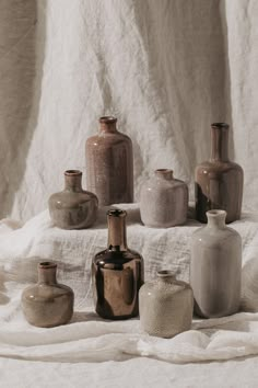 there are many different vases sitting on the table together with white linen behind them