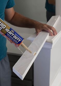 a man is painting the side of a white cabinet with a paintbrush and glue