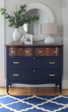 a blue dresser with a mirror and plant on it in front of a white door