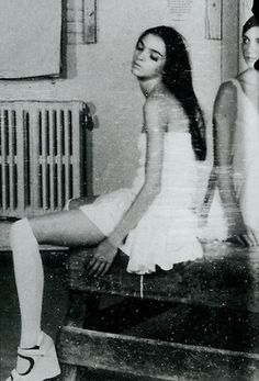 two young women sitting on top of a wooden bench in front of a radiator