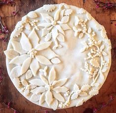 a pie with white frosting and flowers on it sitting on a wooden table next to pink flowers