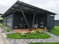 a large black container house with a patio and swing set in the front yard area