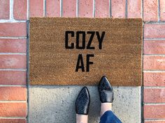 a person standing in front of a door mat that says cozy af