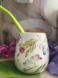 a white cup with flowers painted on it and a green toothbrush in the cup