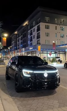 a black car is parked on the side of the road at night in front of some buildings