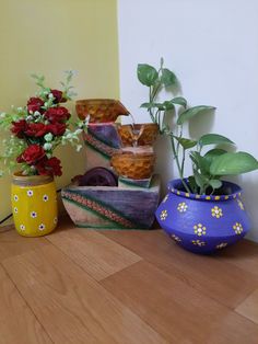 three vases with flowers and plants in them on a table next to a wall