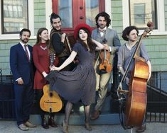 a group of people that are standing in front of a door with guitars and violin