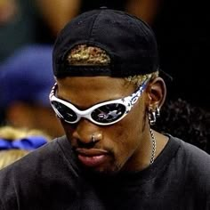 a man wearing sunglasses and a black hat with gold chains on his head is staring at the camera