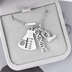 an open box with two necklaces in the shape of lab equipment and letters on it