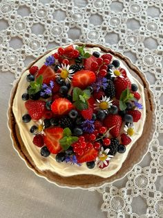 a cake with berries, blueberries and strawberries on top is sitting on a doily