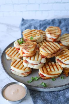 a plate filled with sandwiches on top of a table next to a cup of sauce