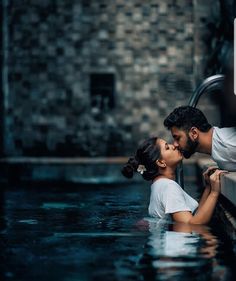 a man and woman kissing in the water next to a wall with a sign on it