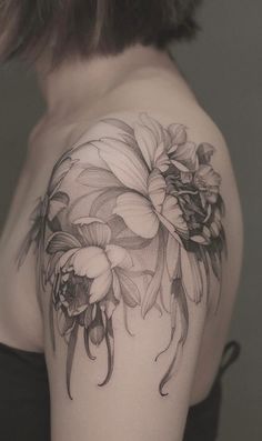 a woman's shoulder with black and white flowers on her left arm, in front of a gray background