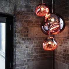 three glass balls hanging from the ceiling next to a brick wall in an industrial building