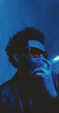 a man wearing sunglasses talking on a cell phone in a dark room with blue lighting