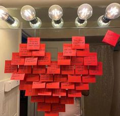 a bunch of red sticky notes attached to a mirror with lights above it and hanging from the ceiling