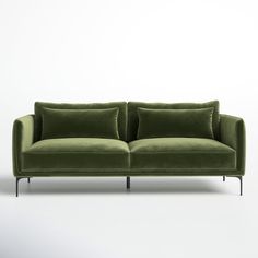 a green velvet sofa with two pillows on it's back and one arm extended to the side