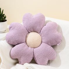 a purple flower shaped pillow sitting on top of a white couch next to a potted plant