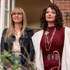 two women standing next to each other in front of a building